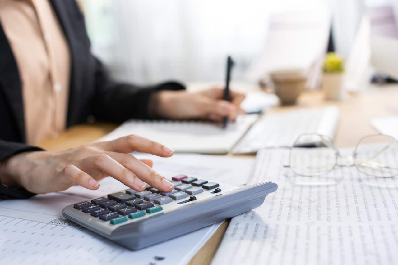 A woman types on a calculator while sitting at desk covered in papers.