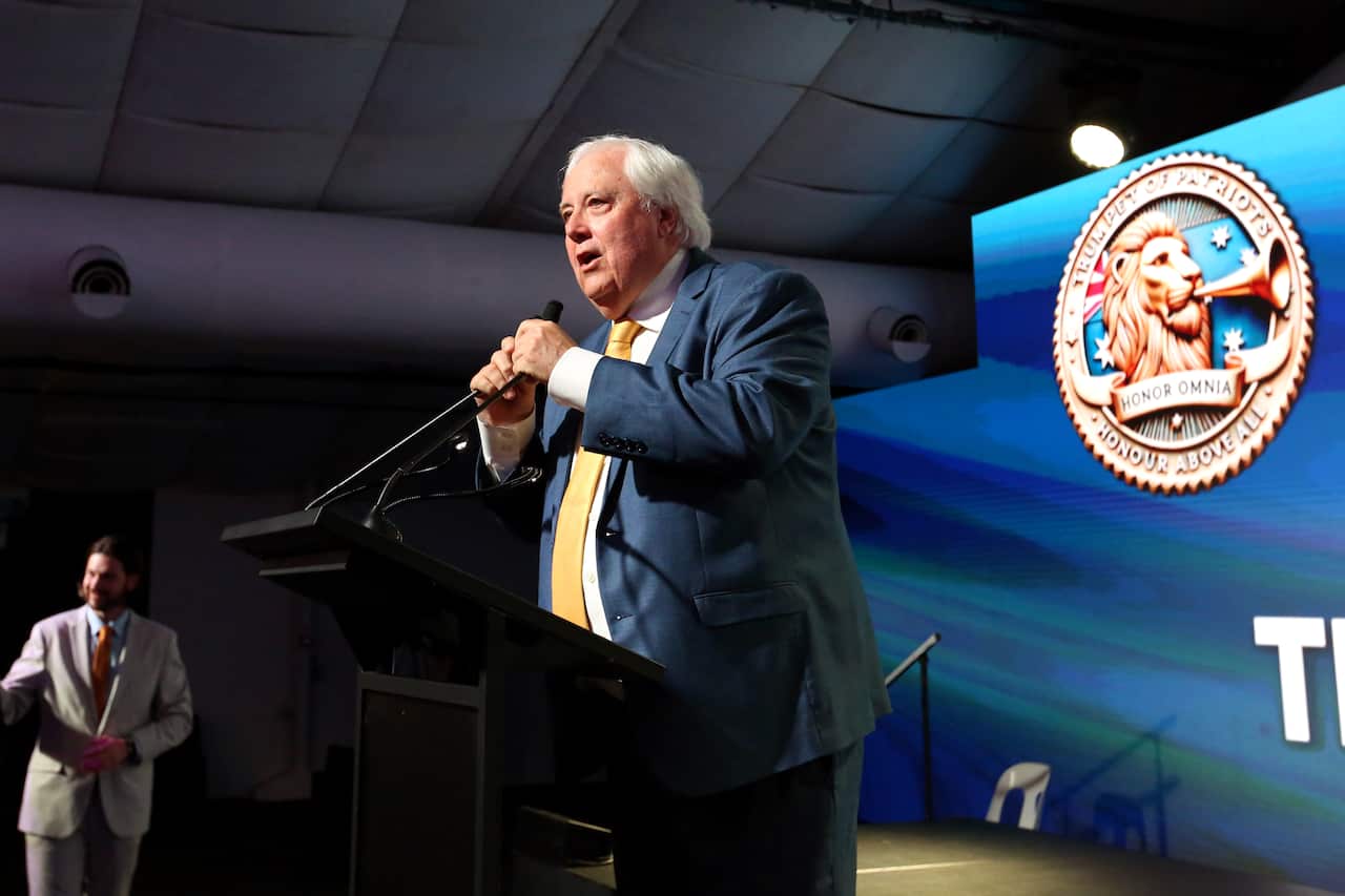 Clive Palmer, wearing a dark suit, speaks into a microphone inside. 