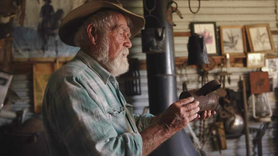 An older man wearing a hat holding an old tin can.
