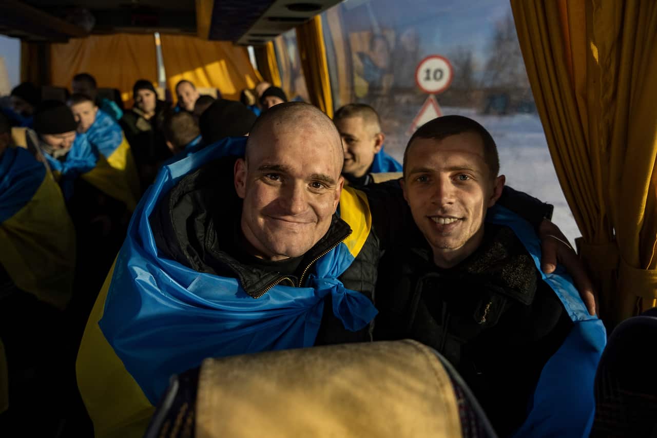 Recently swapped Ukrainian prisoners of war covered in national flags sit in a bus after a prisoner exchange on the Ukrainian Russian border.