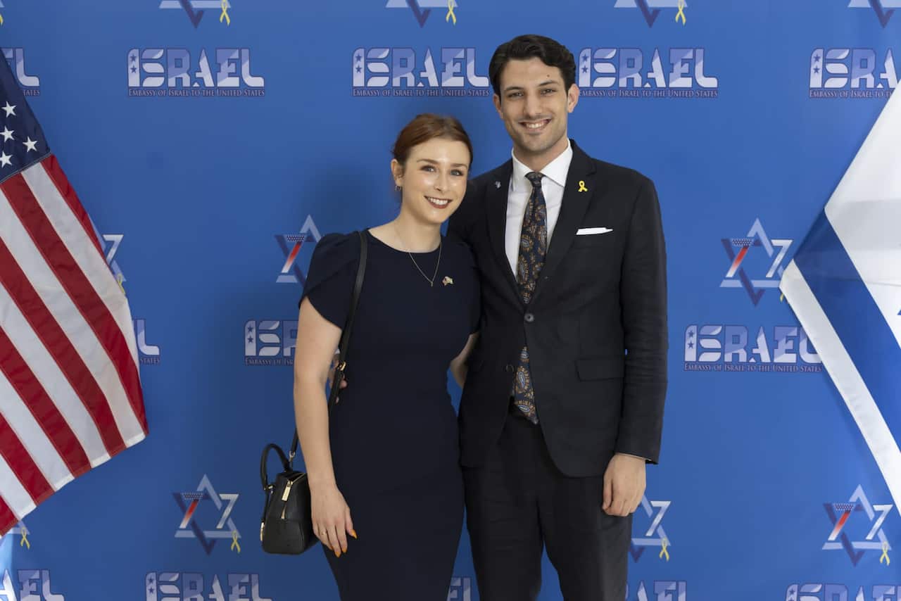 A woman and a man standing in front of a blue background that has the Star of David and the word 'Israel'.