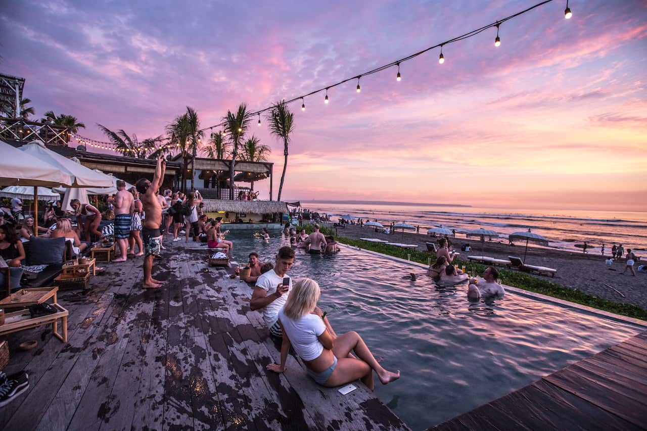 Canggu beach club at sunset, dotted with mostly caucasian tourists taking photos and swimming in the pool.