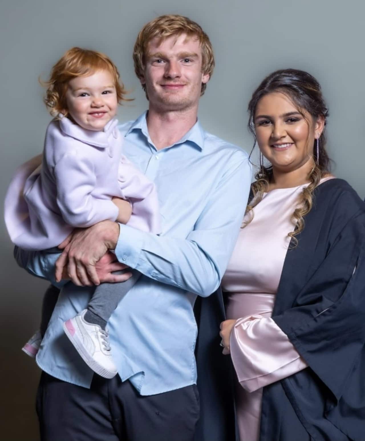 A woman and her husband who is holding their young daughter. They are smiling as they pose for a photo.