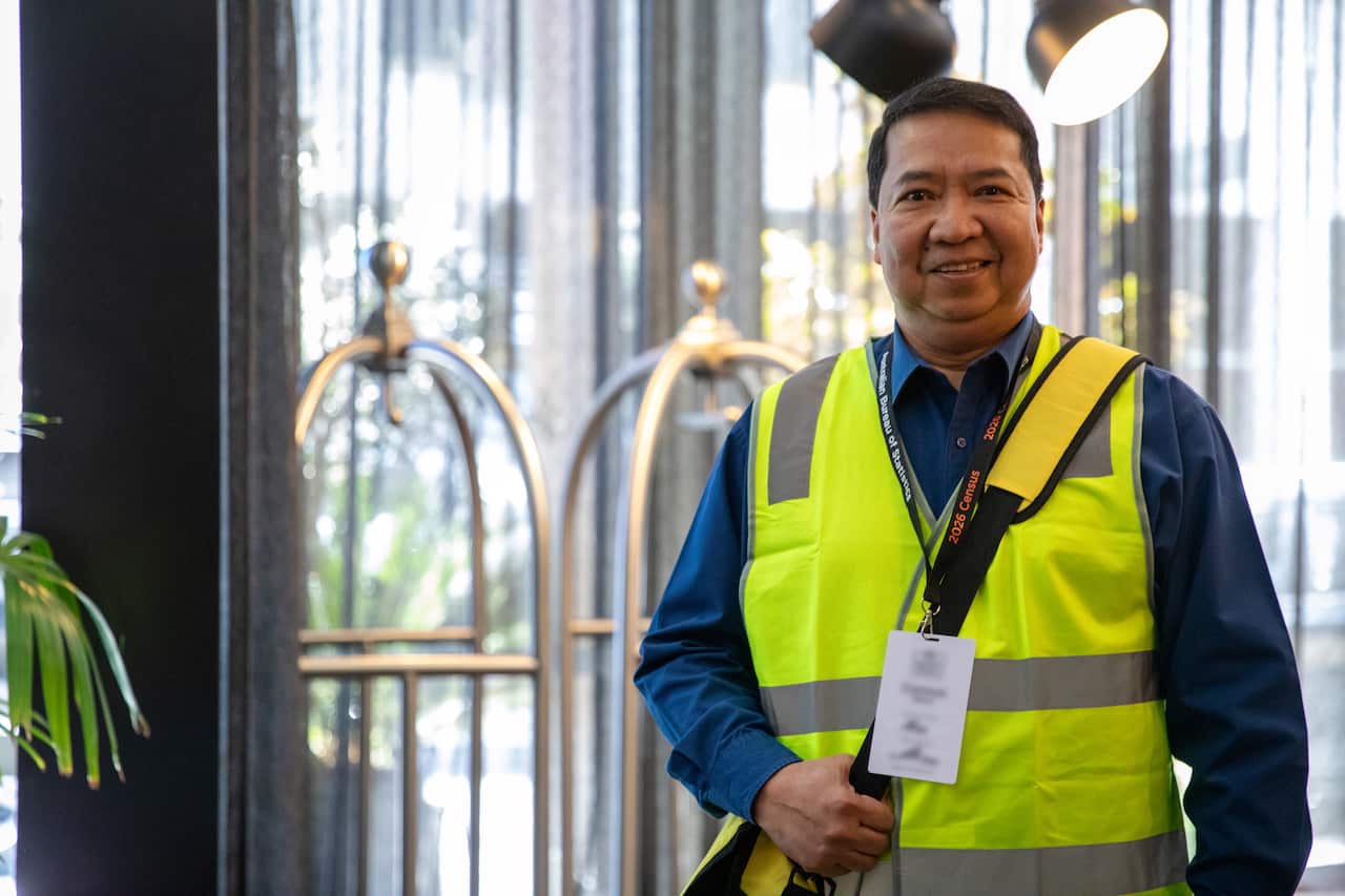 A man wears a navy shirt and fluorescent yellow vest. He has a white lanyard and card around his neck.