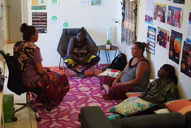 Two women sitting on chairs and two women sitting on the floor in a room 