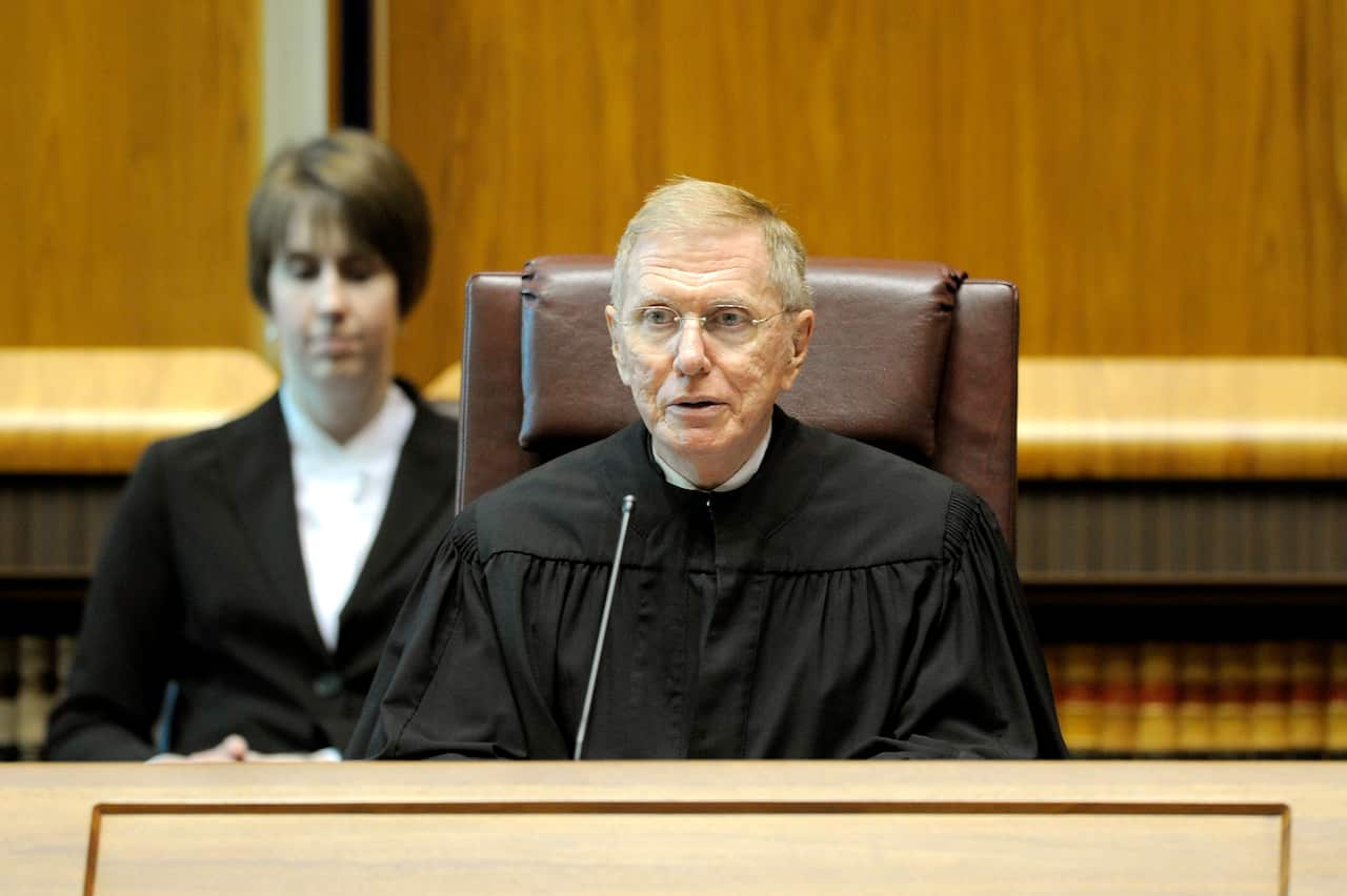 A man in black robes sitting at a court bench speaking into a microphone