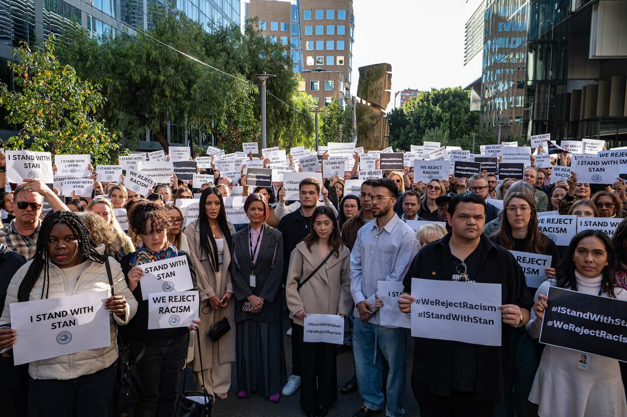 People hold signs reading "we reject racism" and "I stand with Stan"