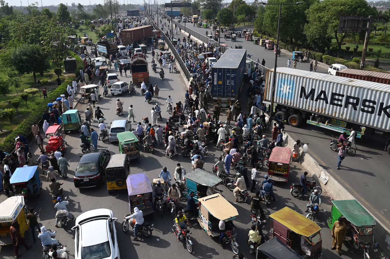 Pakistani commuters try to make their along a road partially blocked with containers by local authorities 