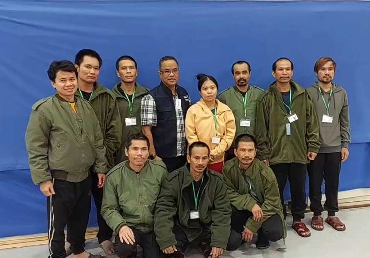 Ten Thai nationals, most of whom wear green military-style jackets, pose for a photo