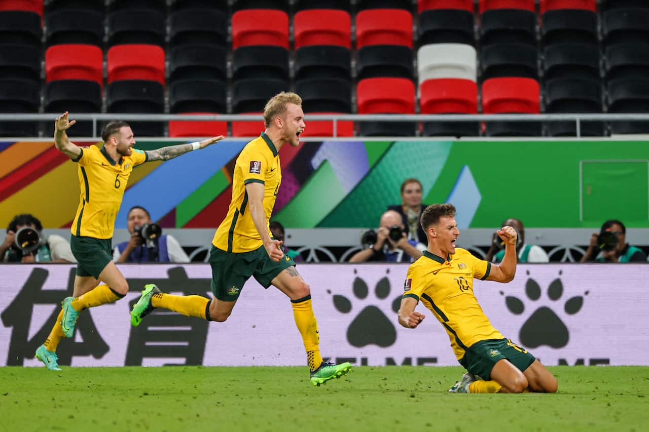 Three Australian football players celebrate on field. On  the left, one has his arms up, the middle is running and yelling, the right is kneeling on the floor with a fist in the air. 