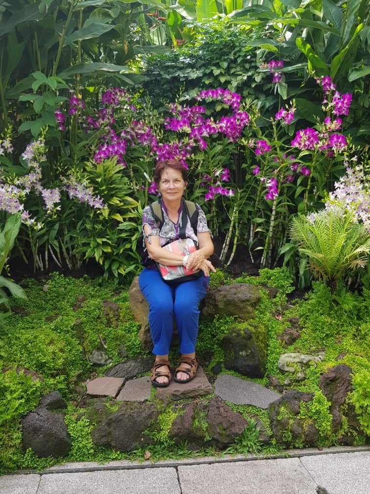 A woman seated on a rock surrounded by lush green foliage.