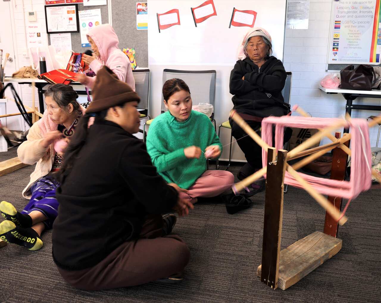 A group of women sit on the floor winding thread onto a hand loom.