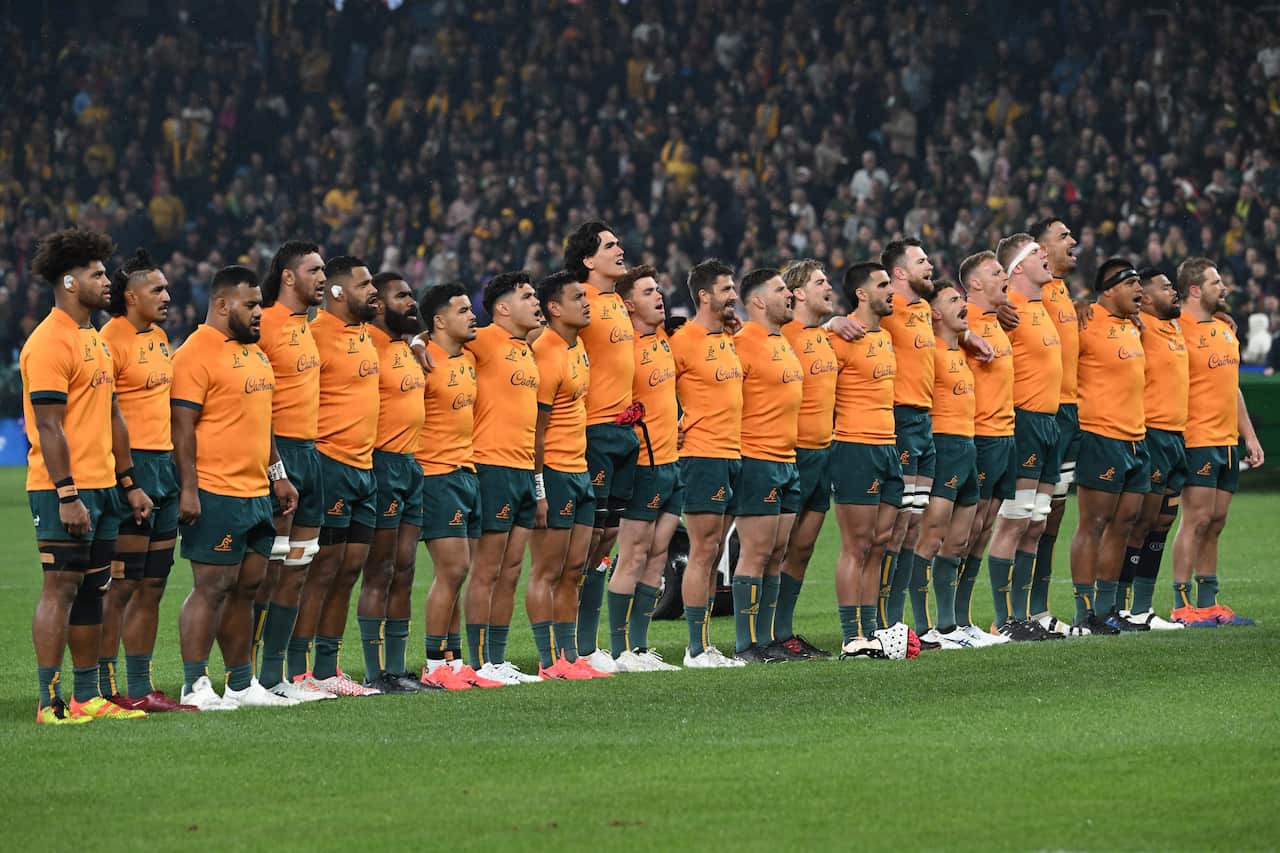 Rugby players wearing gold coloured jeryseys and green shorts line up ahead of a match