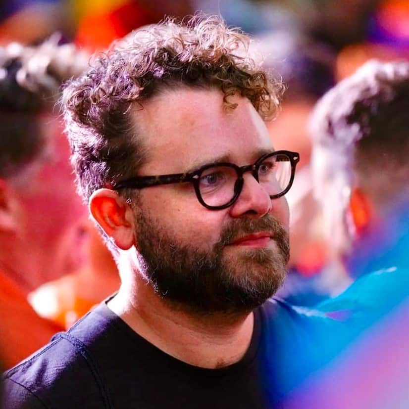 A man with short curly hair, glasses and a beard