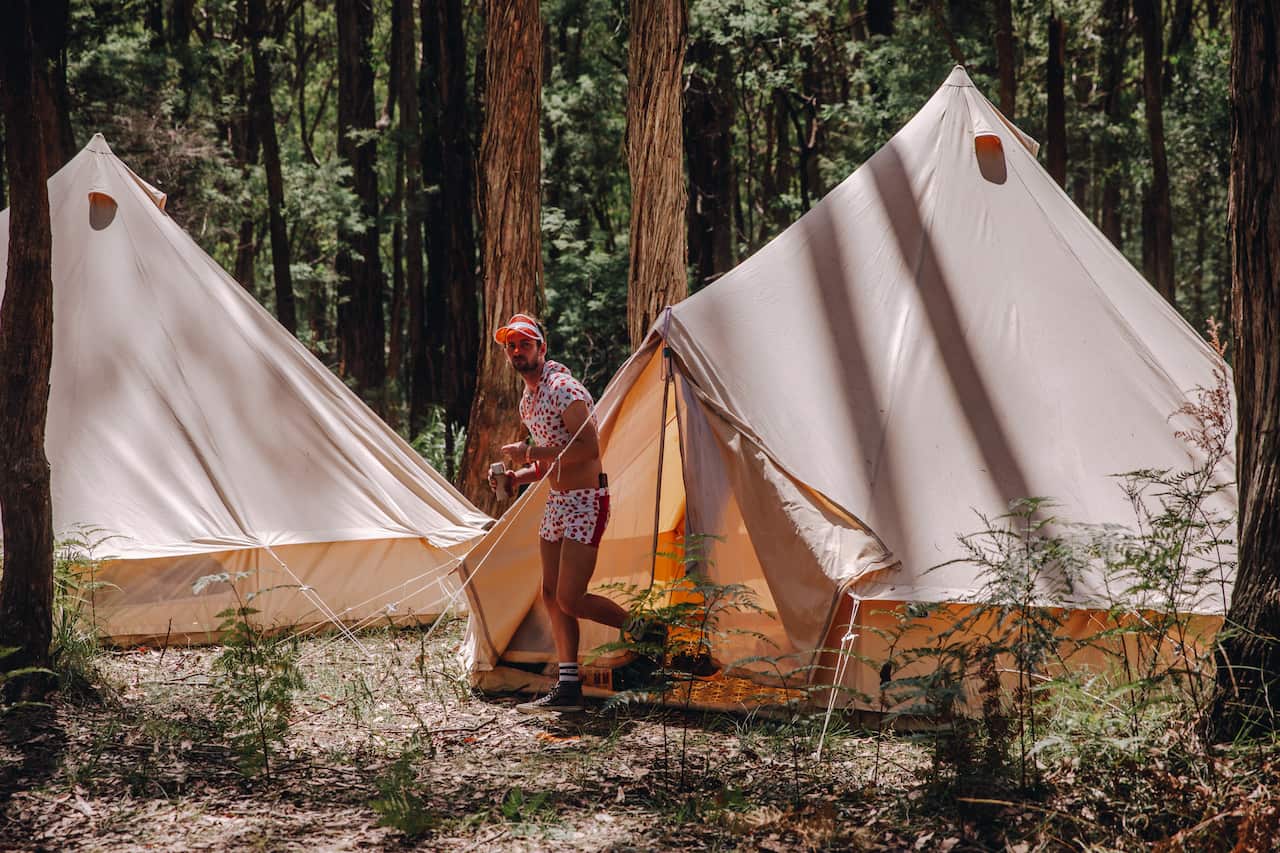 A man in a cute polka dot two piece and transparent orange visor emerges from a glamping-style tent. 