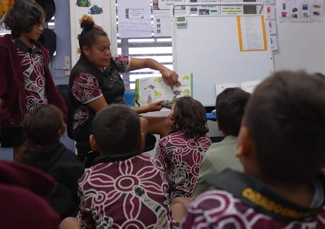 A teacher with a book in a classroom with children