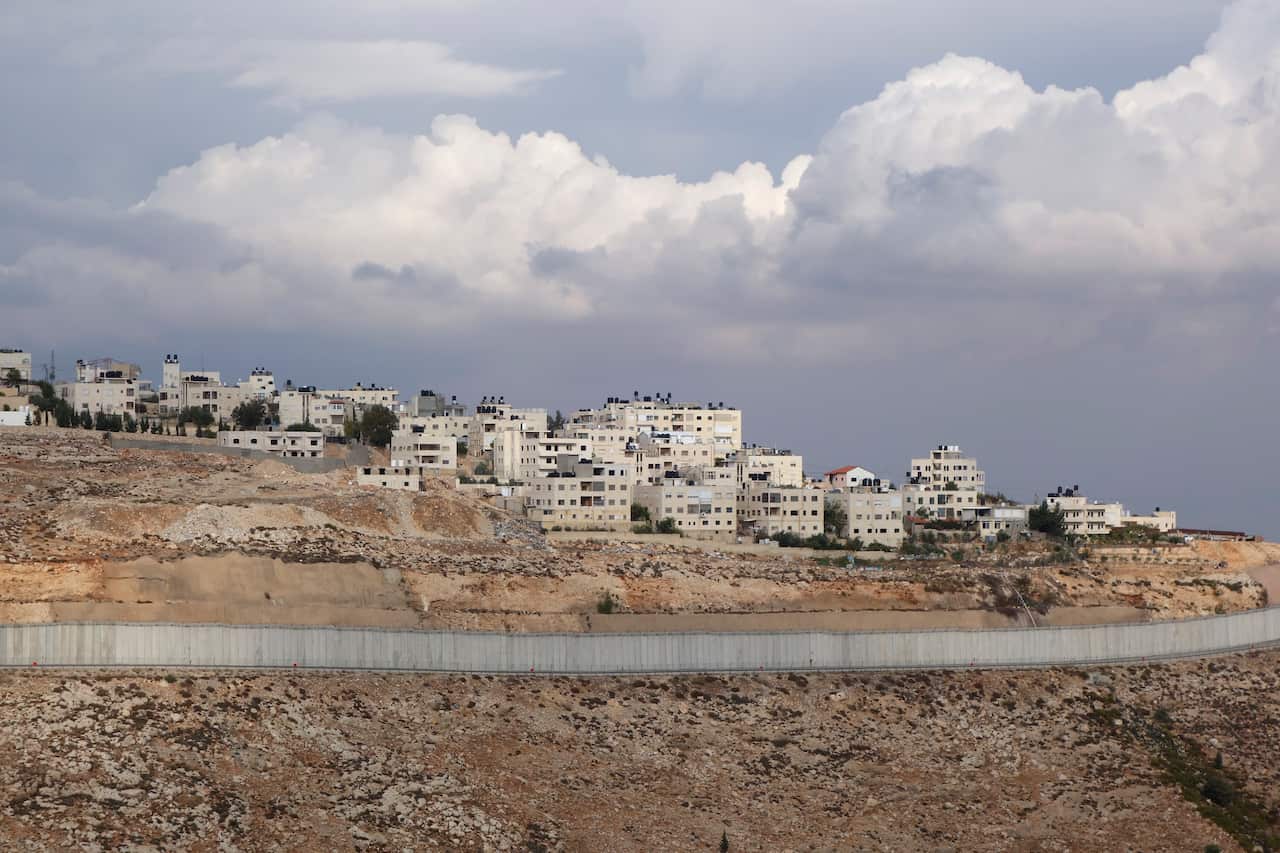 View of the West Bank separation barrier, a large wall, separating a section of land from a section of houses.