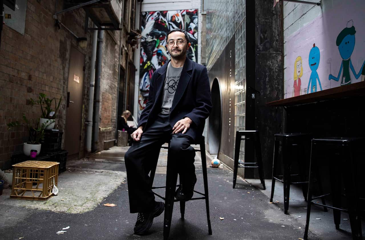 A person sitting on a stool in an alleyway.