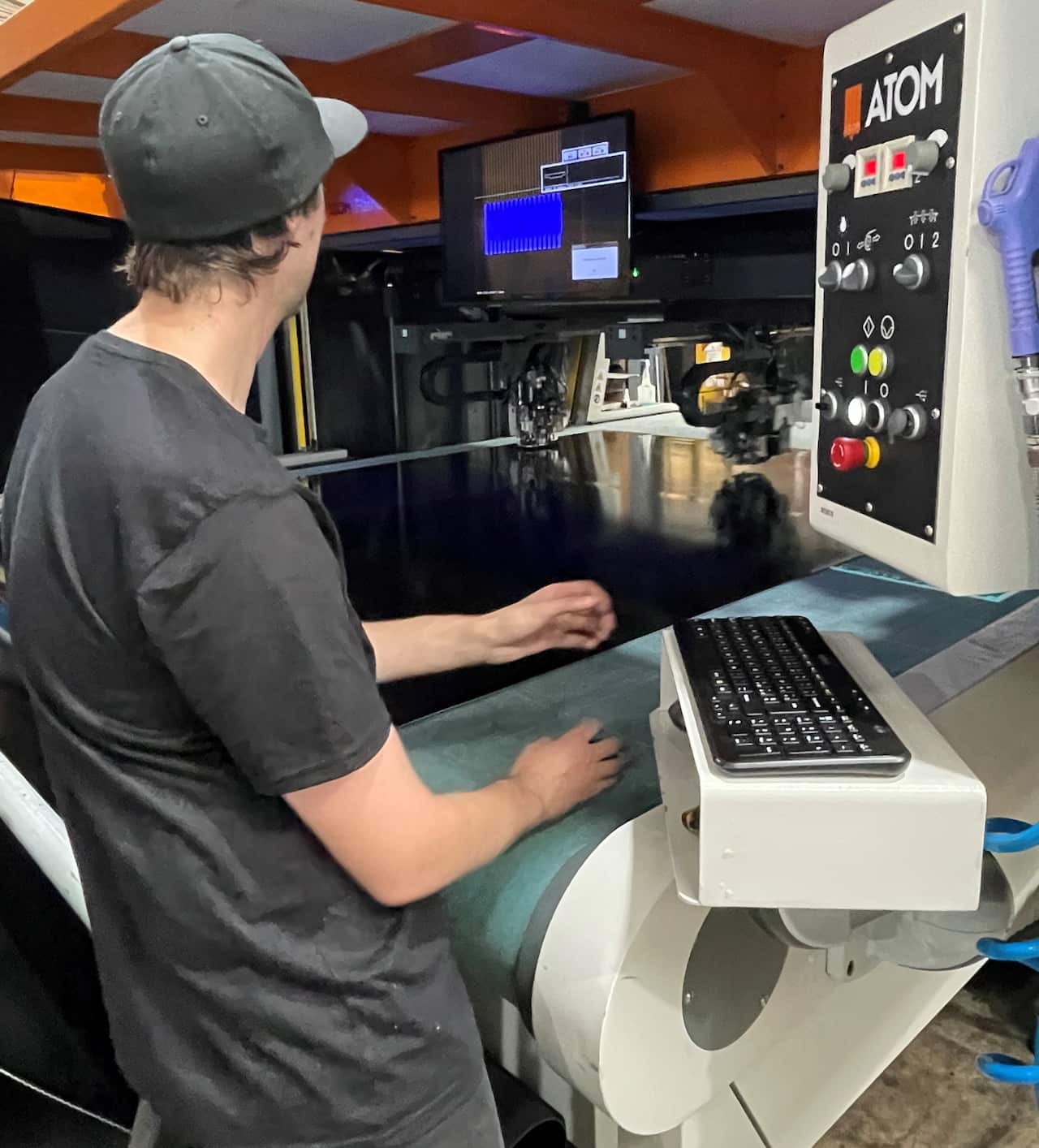 A man sits at a machine cutting leather using computer technology.