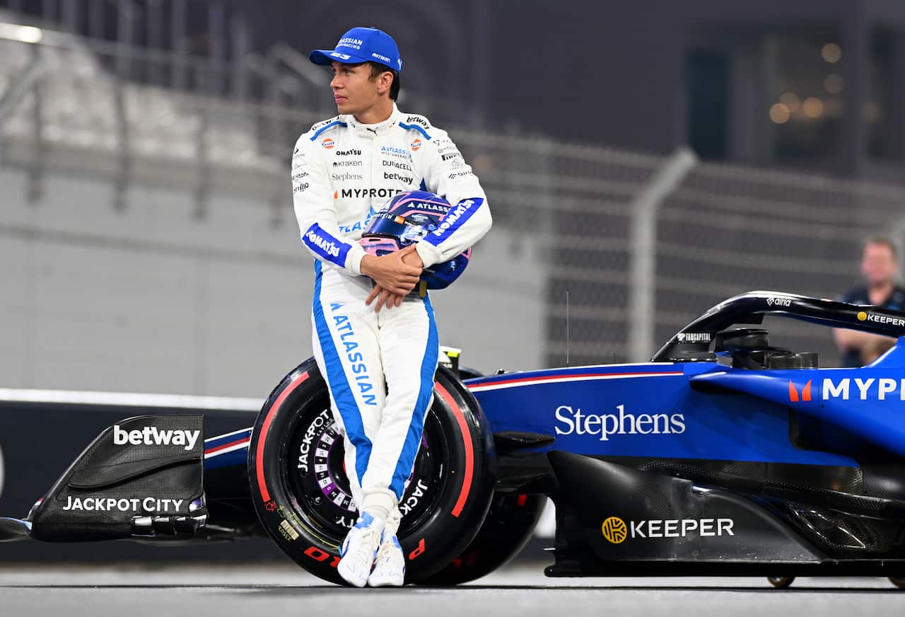 A race car driver leaning against a blue car.