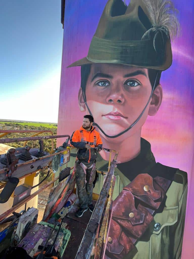 El pintor y escultor Julián Clavijo junto al mural dedicado al soldado adolescente Harold Thomas Bell. 