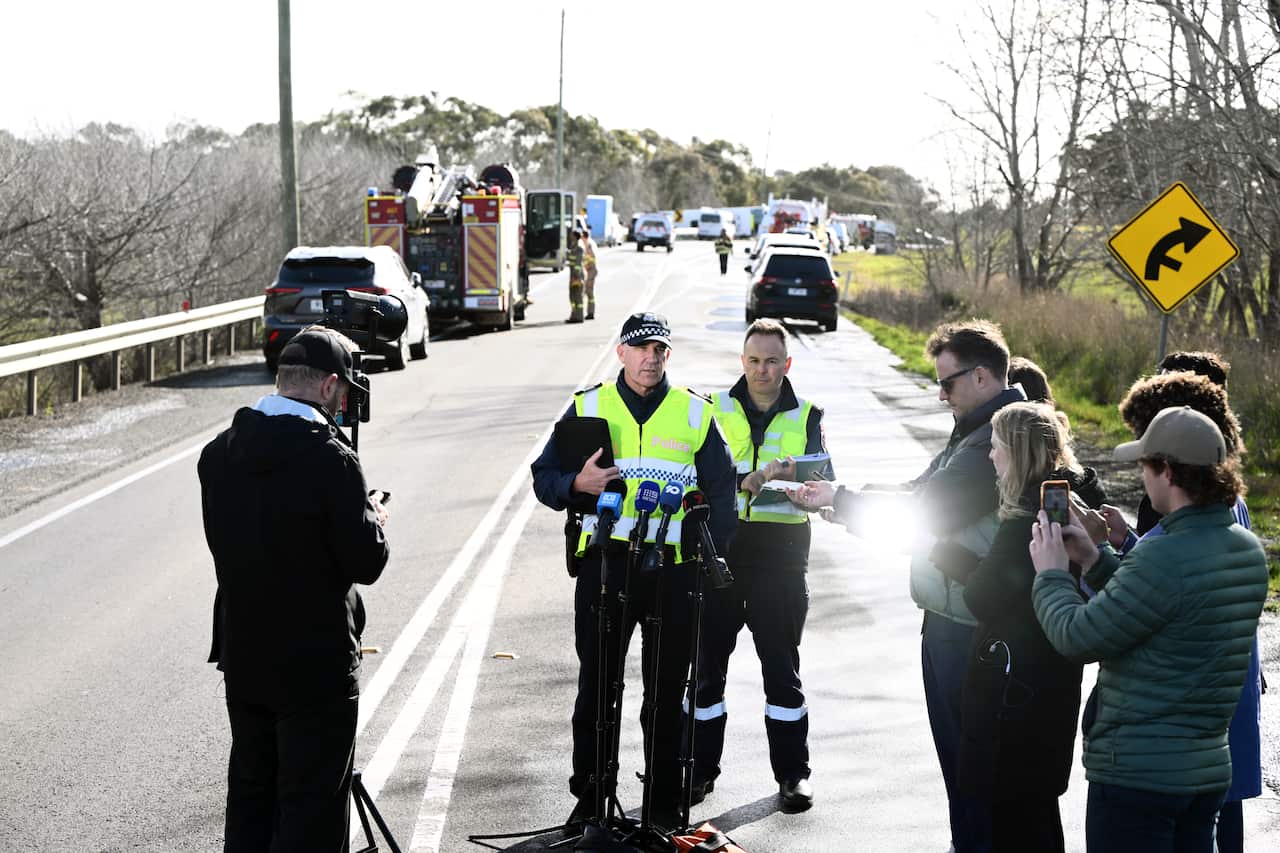 Two men speak to reporters on a road. 