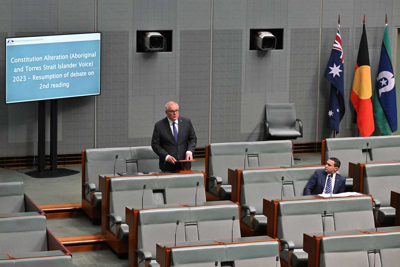A man in a suit speaks as another looks at him.