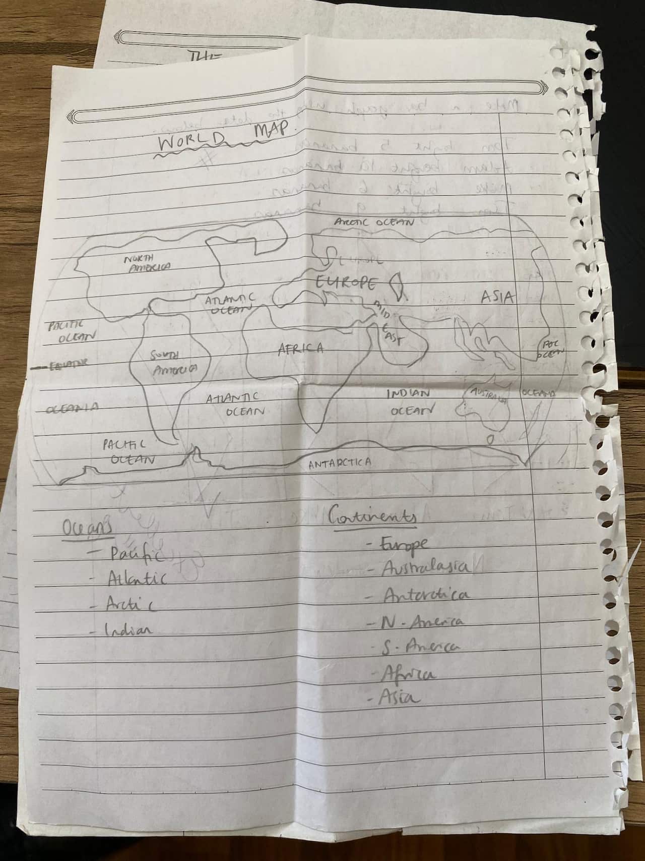 A folded, handwritten school paper shows a simple, hand-drawn world map in pencil, with the continents and major oceans labeled by hand. Below the map, the paper includes two lists titled "Oceans" and "Continents," which are also handwritten in pencil on the lined paper.