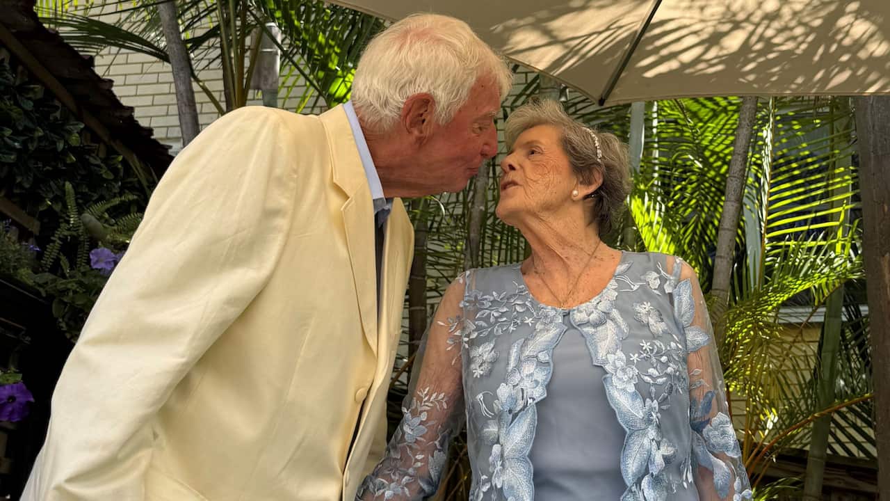 and older man in a white suit kisses an older woman in a blue floral lace outfit on their wedding