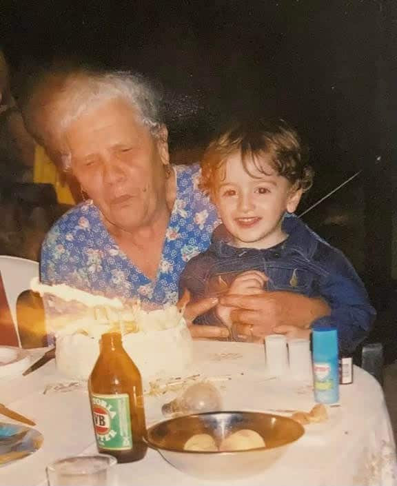 Little boy sitting on old woman's lap blowing out birthday candles together