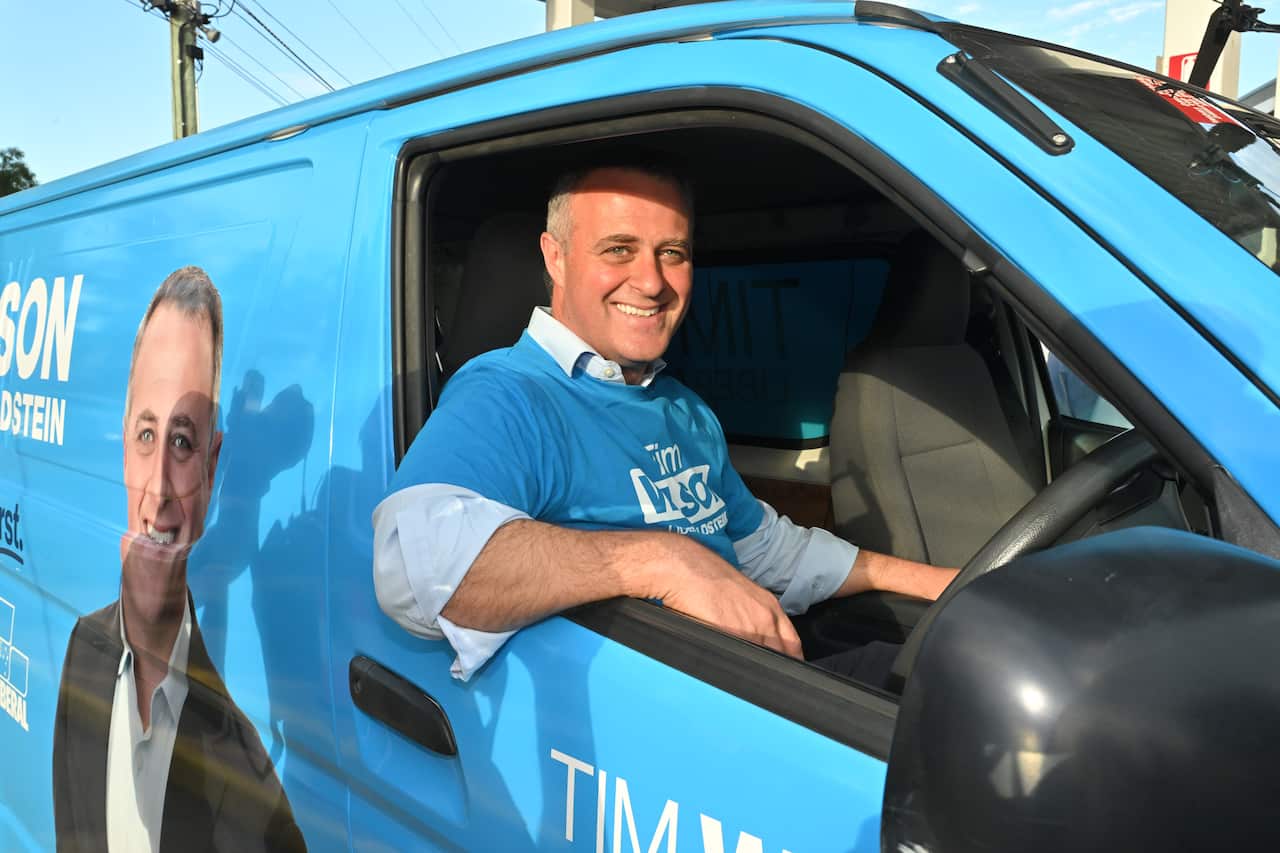 A man sitting in the driver's seat of a blue van smiling with his arm out the window.