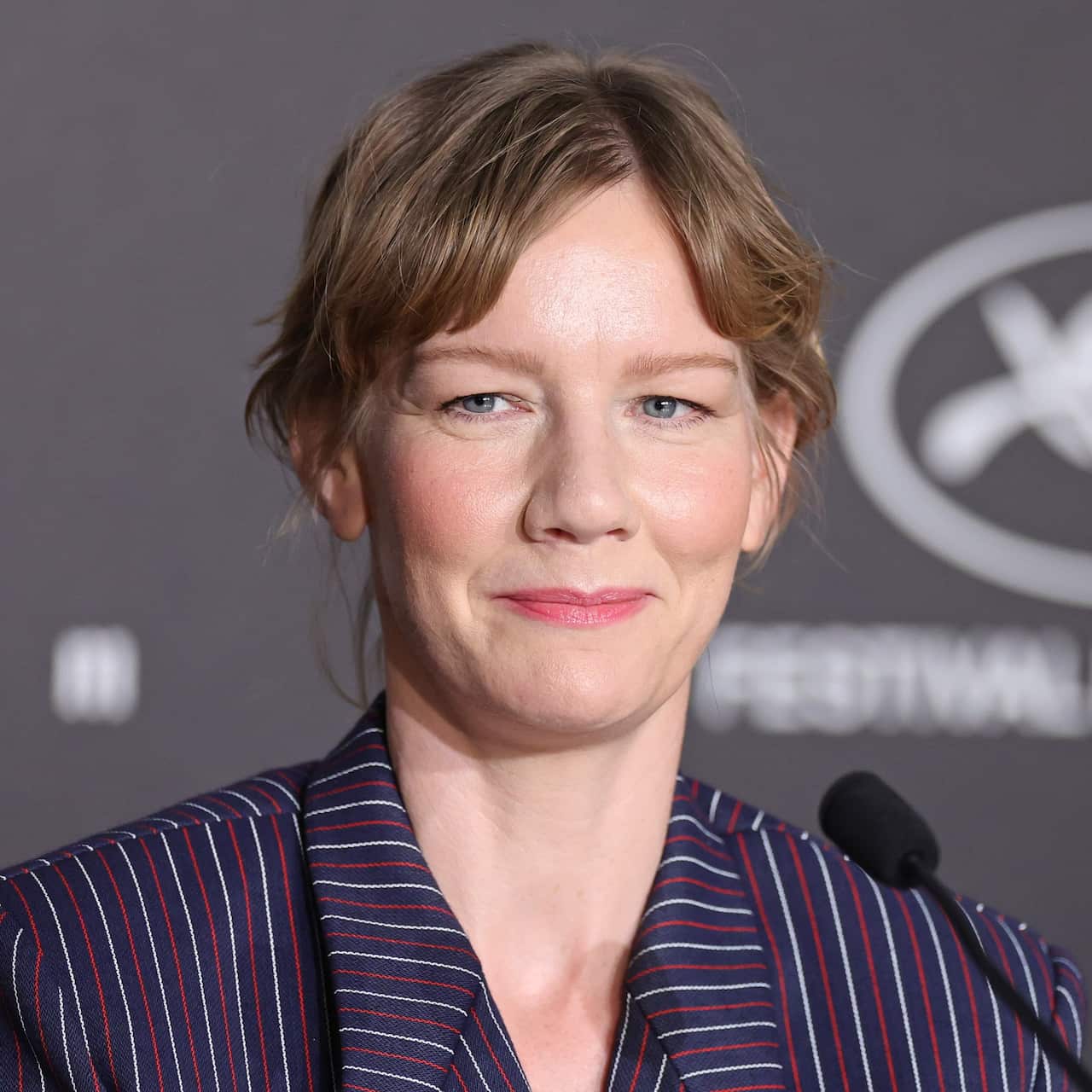 A blonde woman wearing a striped navy, red, and white jackets. A microphone is in front of her