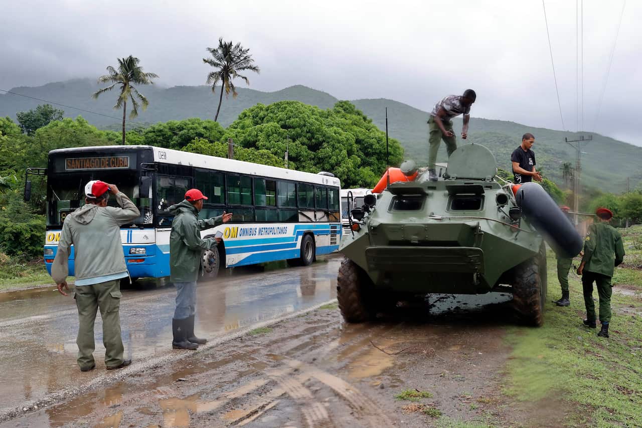 People load tanks and buses along the road in the rain.