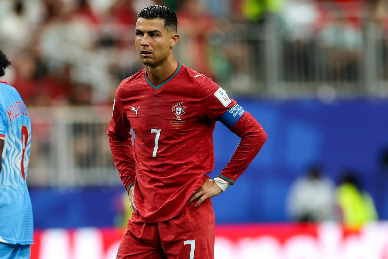 Cristiano Ronaldo, wearing red football shirt and shorts, stands with his hands on his hips on the field
