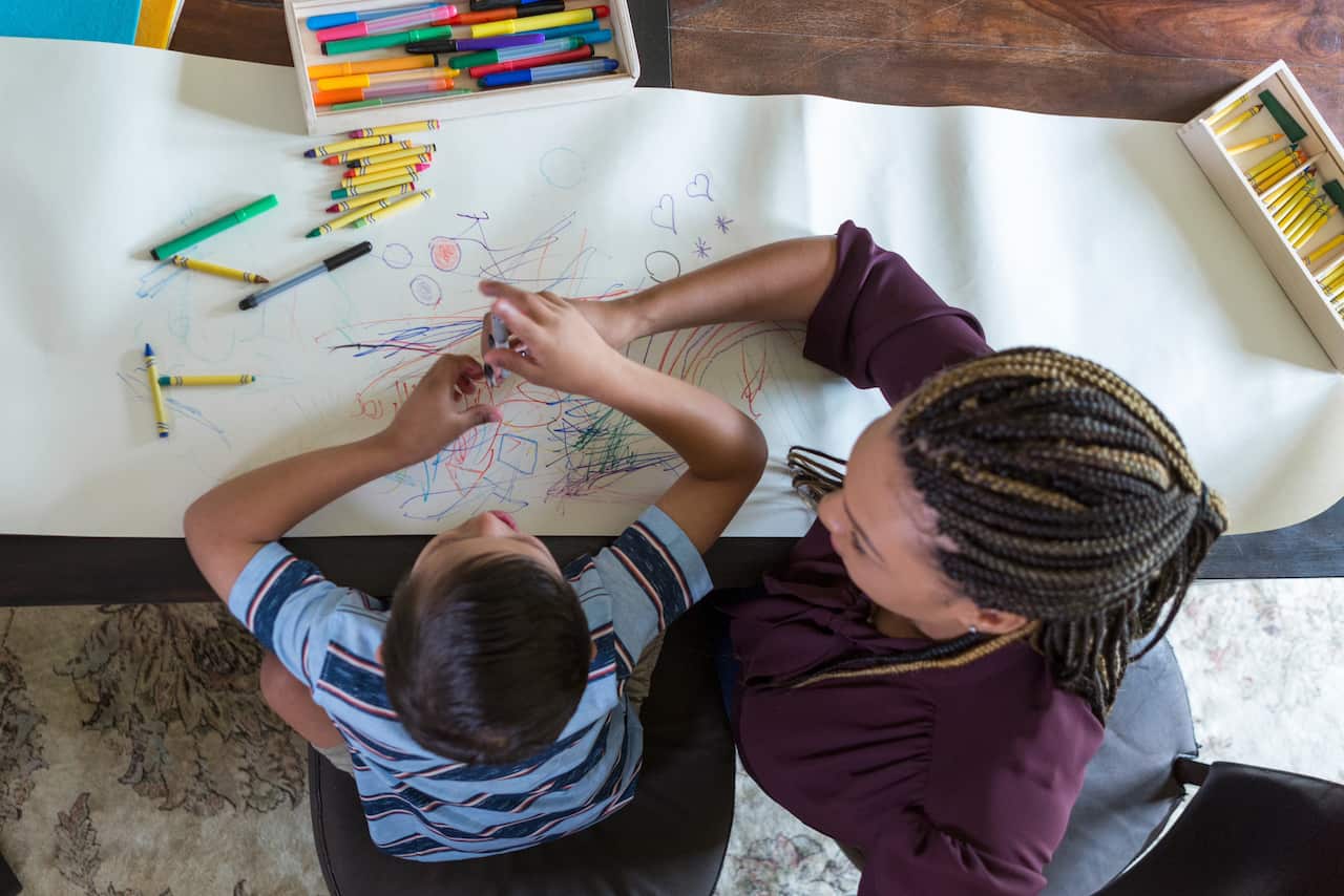 A child colouring with crayons while sitting next to a woman.