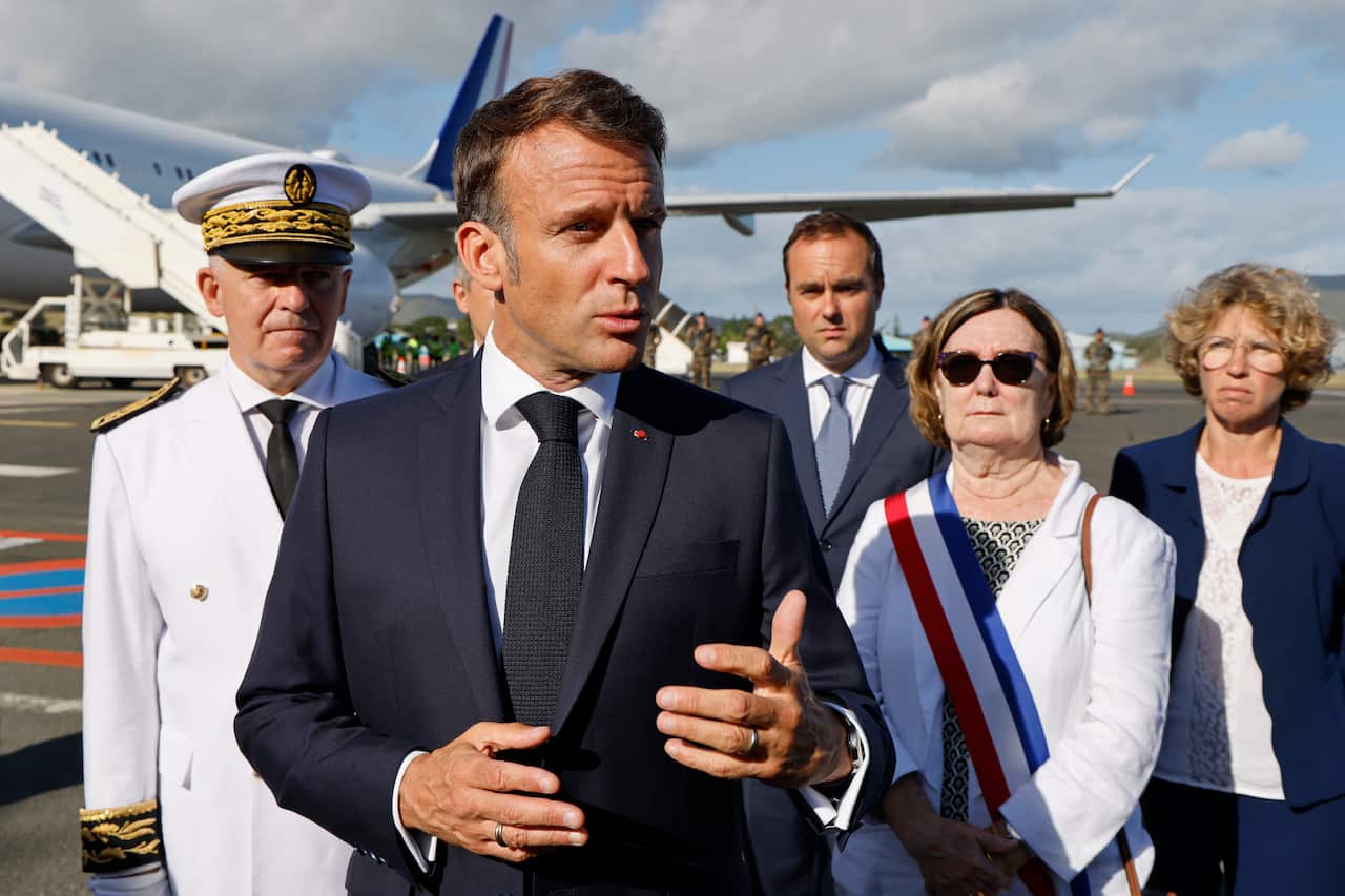 A man in a suit speaking to media in front of a plane