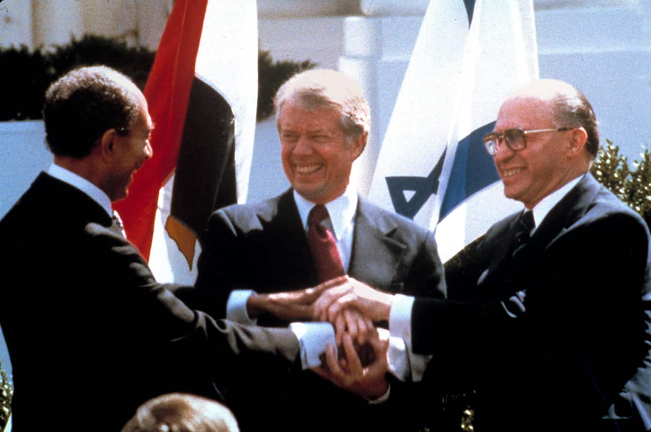 Three men wearing suits smile as they clasp their hands.