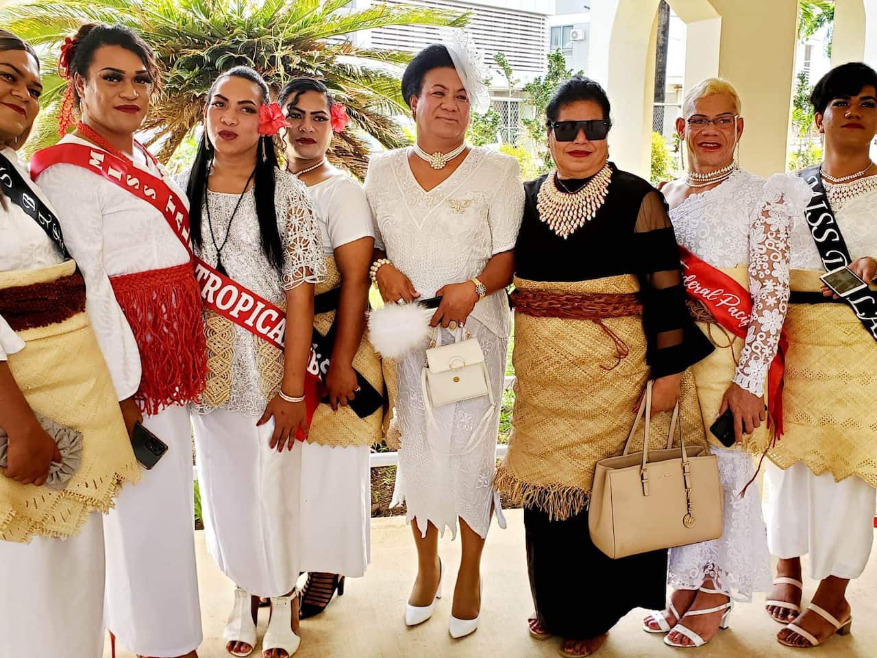 Seven people in white dresses and traditional Tongan garments, and one in black.
