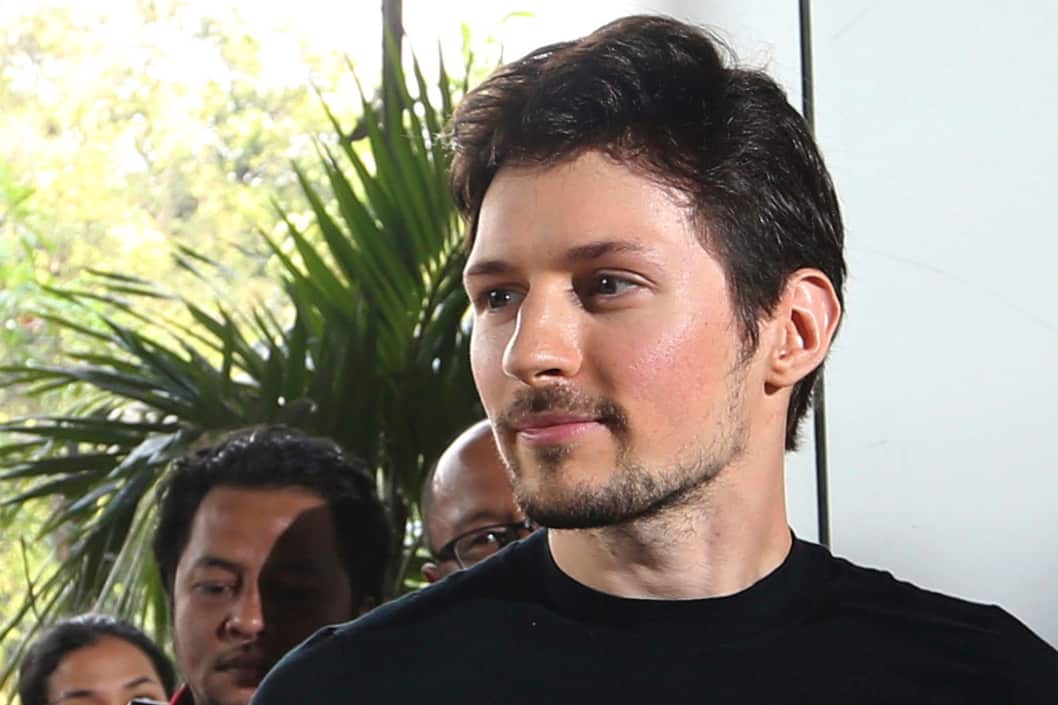 Man in black shirt looks to the side in front of white wall and trees