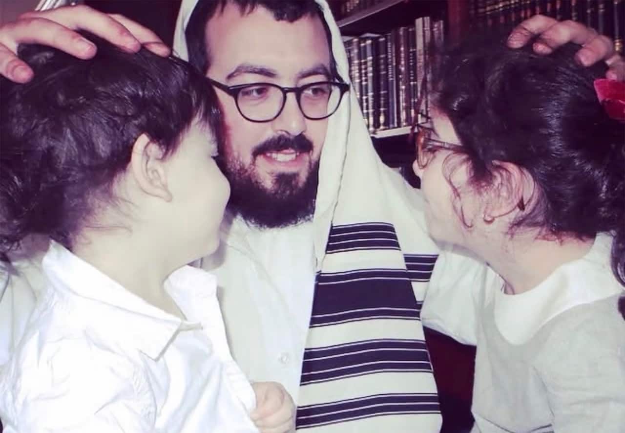 A rabbi putting his hands on the heads of two children.
