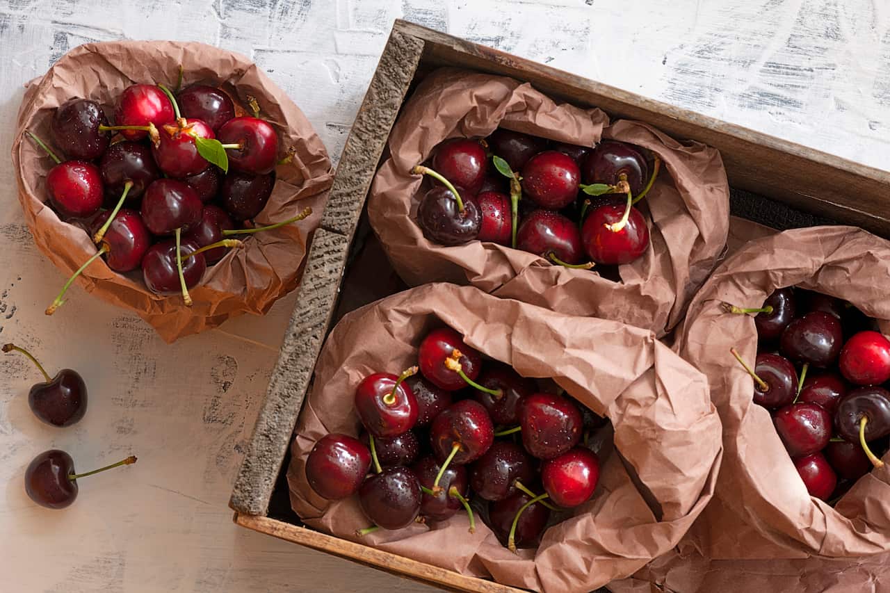 Cherries in paper bags in a old wooden box on white background