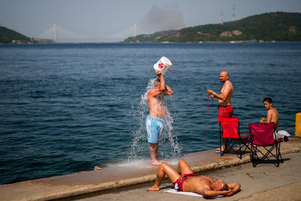 People cooling off by the water, one person throwing a bucket of water over their head.