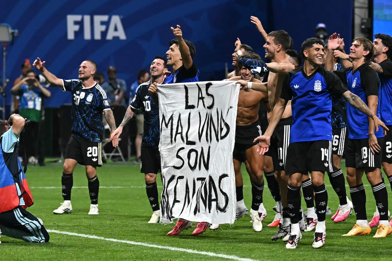 Argentinian footballers celebrate their win and hold a white bedsheet with the words Las Malvinas Son Argentinas painted on it