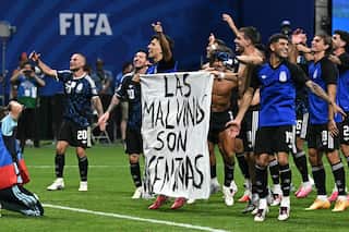 Argentinian footballers celebrate their win and hold a white bedsheet with the words Las Malvinas Son Argentinas painted on it