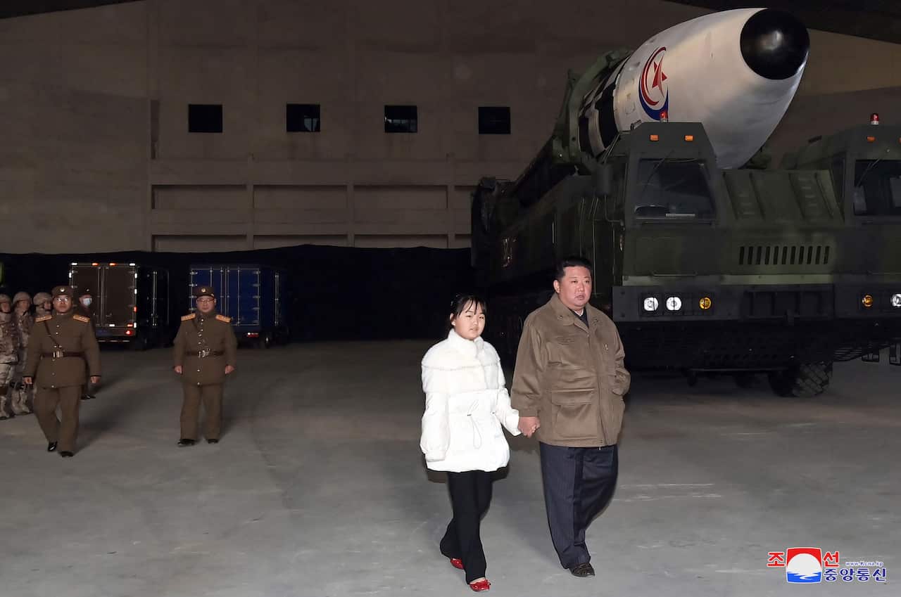 A man walks with a young girl in front of a new ballistic missile in North Korea. 