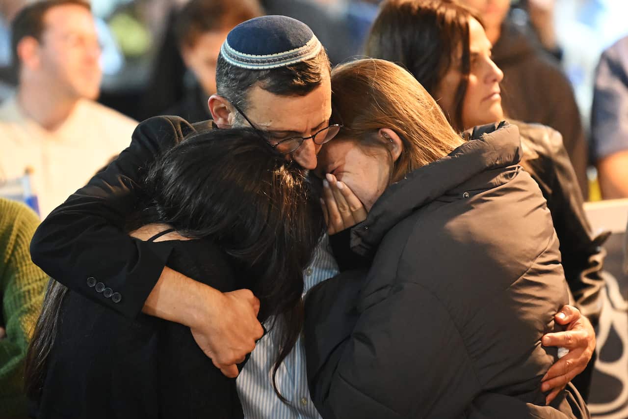A man and two women join in a sad and emotional embrace. 