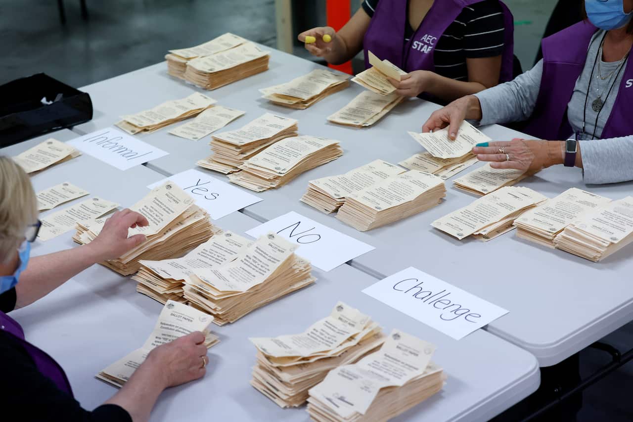 Piles of ballot papers on a table being counted by people sitting at the table