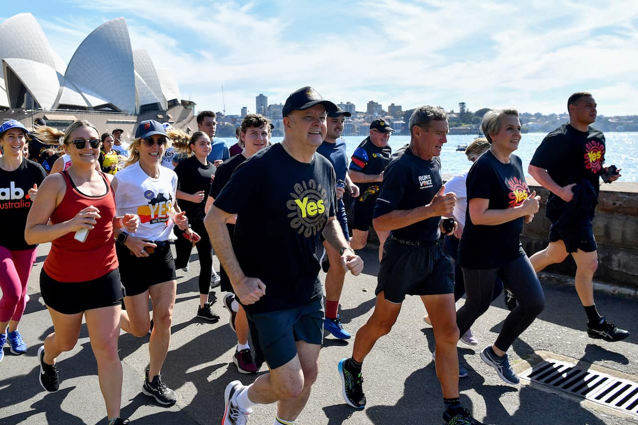 A group of people, many wearing shirts that say 'Yes', running along a path. The Sydney Opera House is in the background.