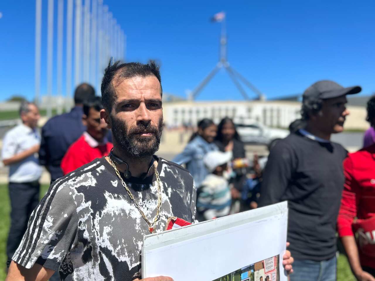 Man with a beard in a t-shirt and necklace holds a sign.