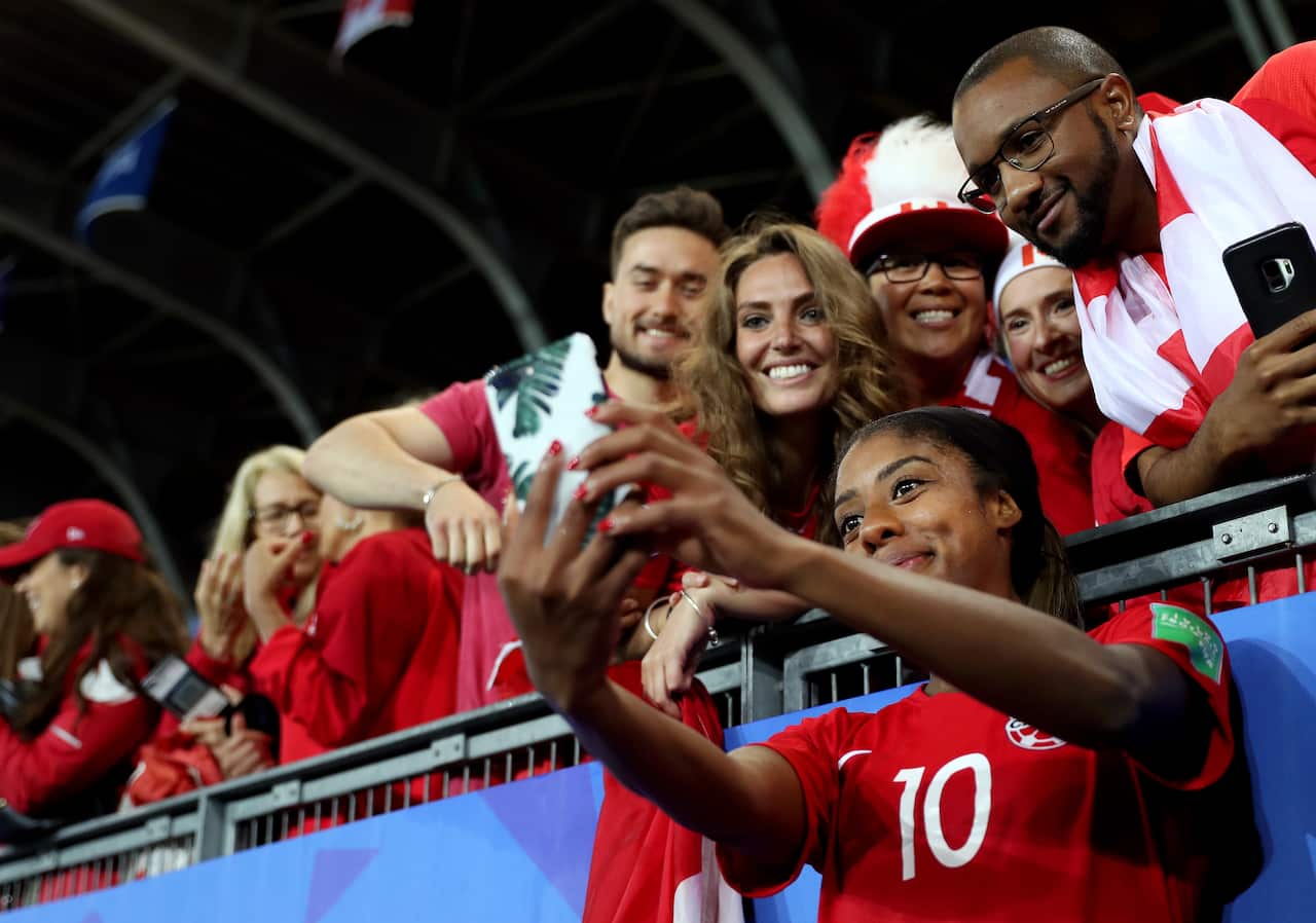 A female footballer poses for a selfie with fans after a match.